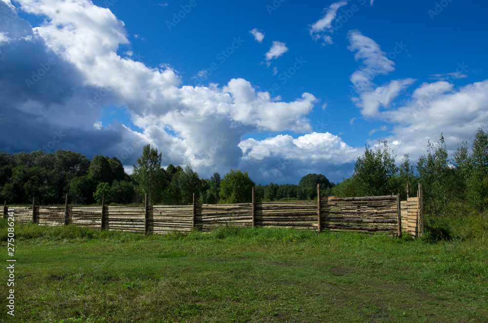 Wooden fence set in a forest area in the background of a blue sky with clouds