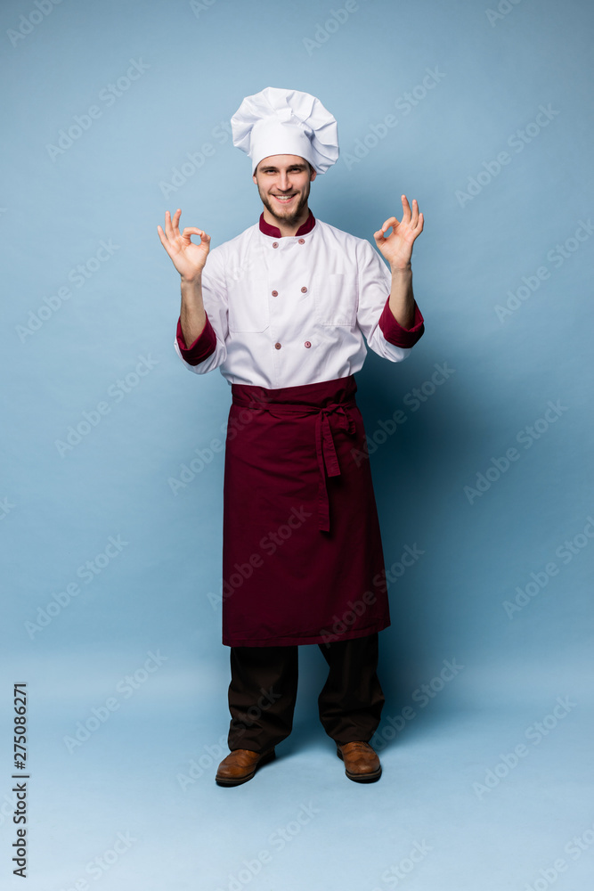 Positive professional happy man chef showing tasty ok sign isolated on light blue. Positive professional happy man chef showing tasty ok sign isolated on light blue.