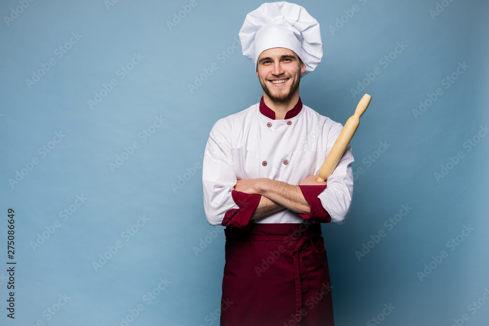 Naklejka premium Portrait of positive toothy chef cook in beret, white outfit having tools in crossed arms looking at camera.
