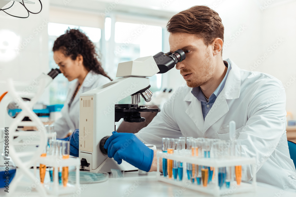 Handsome young man looking into the microscope Handsome young man looking into the microscope