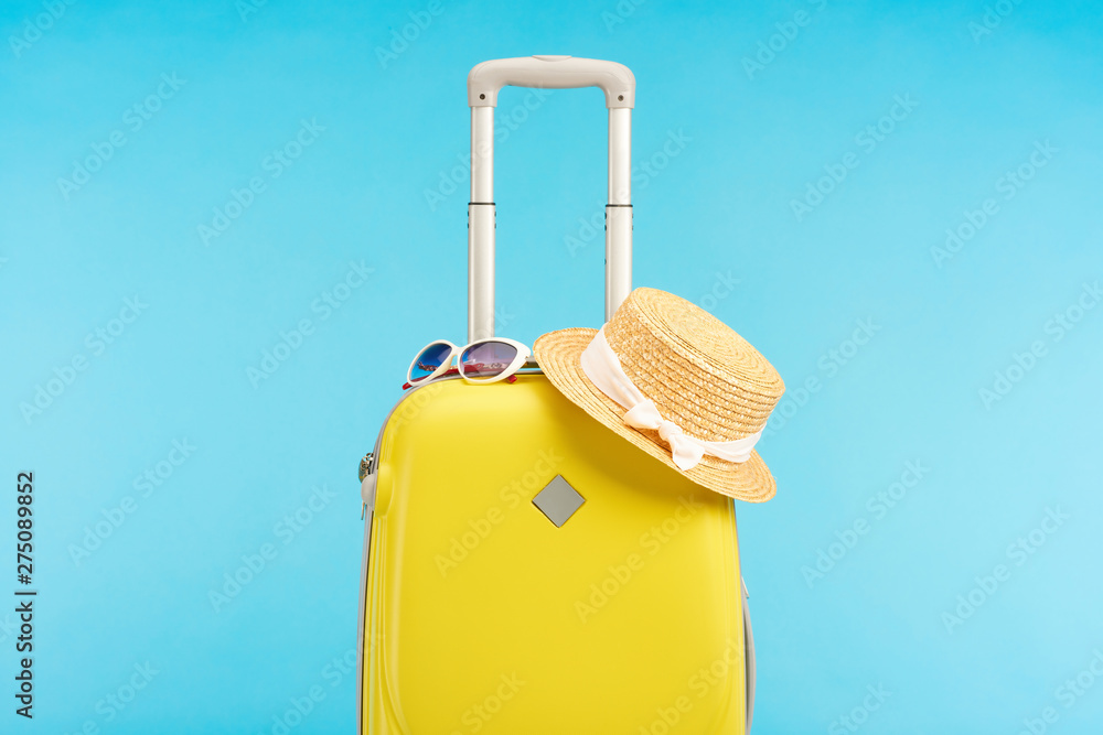 yellow colorful travel bag with straw hat and sunglasses isolated on blue - obrazy, fototapety, plakaty 
