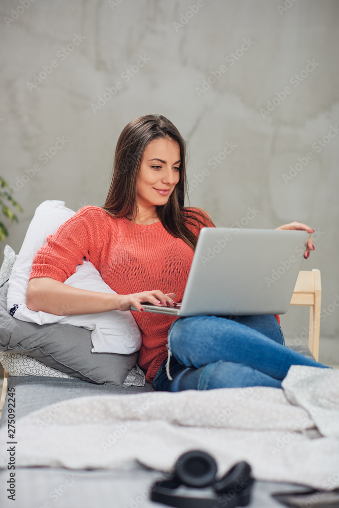 Beautiful Caucasian brunette sitting on the bed in bedroom and using laptop. Beautiful Caucasian brunette sitting on the bed in bedroom and using laptop.
