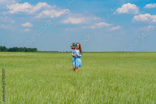 A happy girl with long hair is standing on the grass on a green field with a bright windmill in her hands. Concept of summer, freedom and happy childhood.