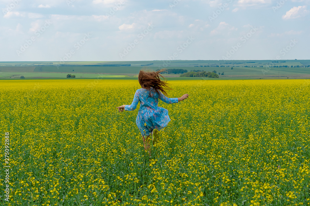A happy girl with long hair runs across a yellow flower field. Hair develop. Yellow flowers. Concept of summer and happy childhood. A happy girl with long hair runs across a yellow flower field. Hair develop. Yellow flowers. Concept of summer and happy childhood.