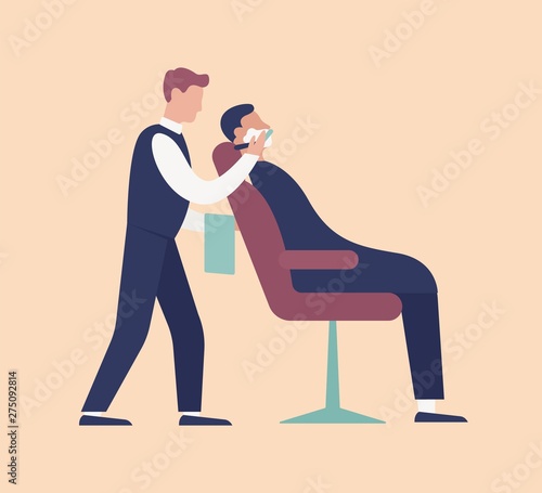 Barber putting foam and shaving young man sitting on chair