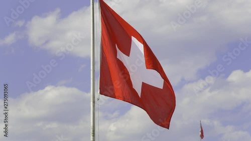 Flag of Switzerland waving in the wind against blue sky with white clouds