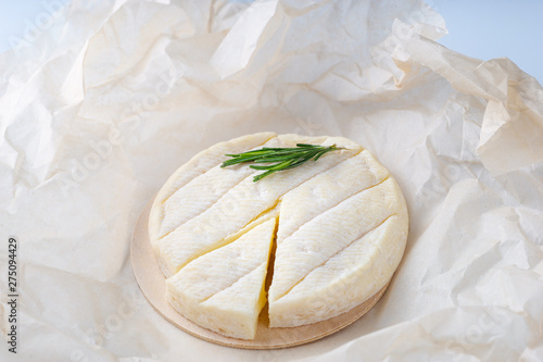 Fresh Brie cheese and a slice on a wooden board with freshrosemary branch photo