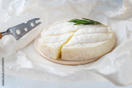 Fresh Brie cheese and a slice on a wooden board with freshrosemary branch photo