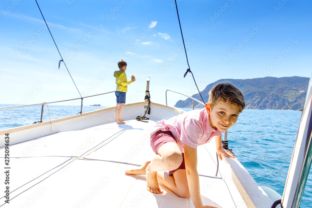 Two little kid boys, best friends enjoying sailing boat trip. Family vacations on ocean or sea on sunny day. Children smiling. Brothers, schoolchilden, siblings, best friends having fun on yacht.