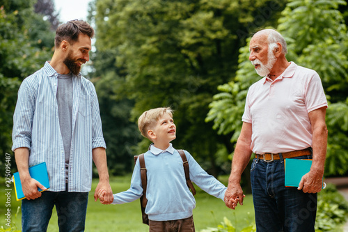 Boy with father and grandfather outdoor over park on background. Three generarion family concept. Parent take child to school. Pupil of primary school go study with backpack. © Iryna