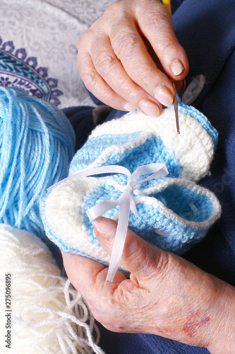 Grandma's hands are holding blue and white yarn and baby booties