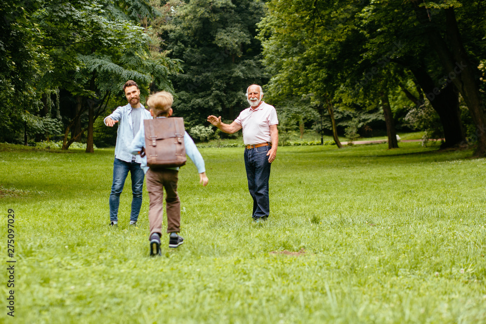 Dad and granddad meets their son from elementary school. joyful child runs into the arms of his parents. Raer view of happy schoolboy runs towards his father and grandfather. the end of the school day Dad and granddad meets their son from elementary school. joyful child runs into the arms of his parents. Raer view of happy schoolboy runs towards his father and grandfather. the end of the school day
