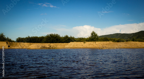 Summer landscape, forest and lake in green grass and sand, mountains and cloudy sky. summer in Russia.