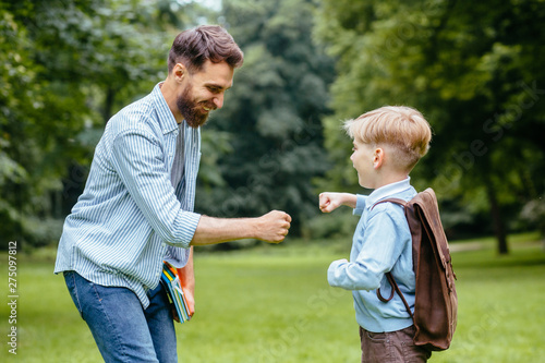 Image of a modern beard father giving a hi-five his little son in the park. Dad meets his son from elementary school. the end of the school day concept. © Iryna