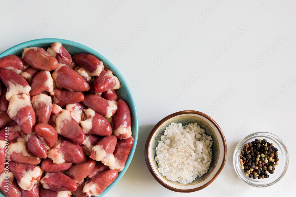 Fresh raw chicken hearts on white background. Organ meats, salt and pepper, cooking ingredients. Top down view, horizontal, copy space. Fresh raw chicken hearts on white background. Organ meats, salt and pepper, cooking ingredients. Top down view, horizontal, copy space.