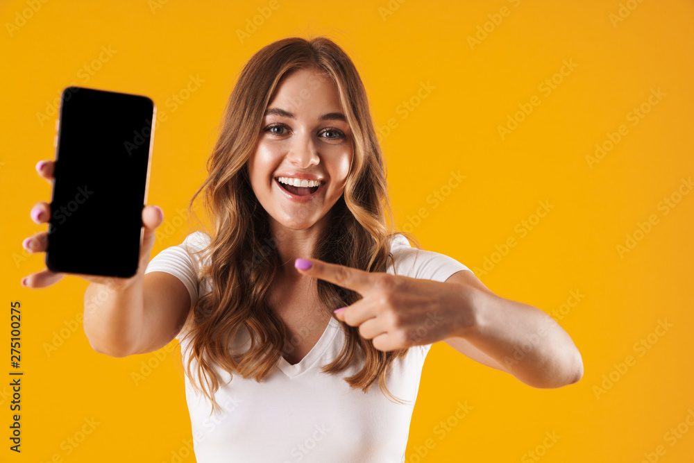 Image closeup of young caucasian woman wearing basic t-shirt rejoicing while pointing finger at cellphone - obrazy, fototapety, plakaty 