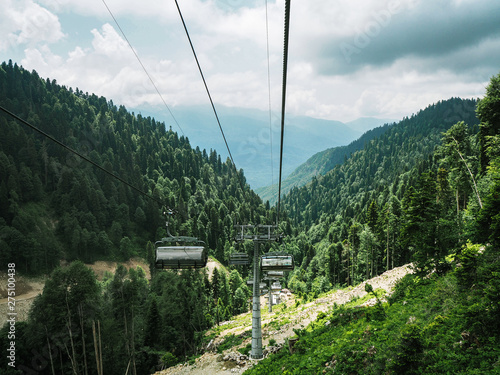 Chairlifts at mountains and forest background at cloudy summer day