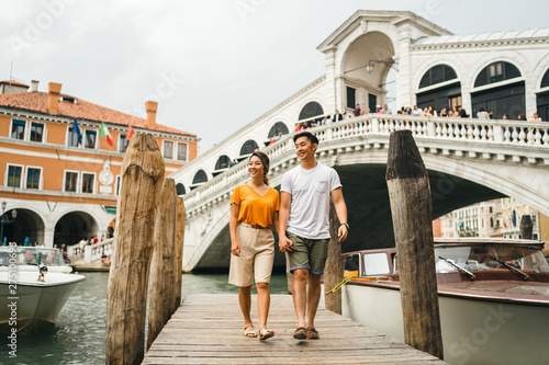 Loving couple on vacation in Venice, Italy - Millennials visiting the famous Rialto Bridge while walking on the wooden pier