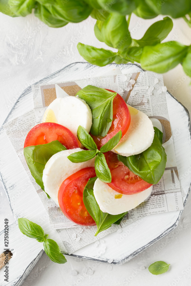Caprese salad with mozzarella, juicy tomato and fresh Basil. Delicious Italian snack, traditional food. On light background