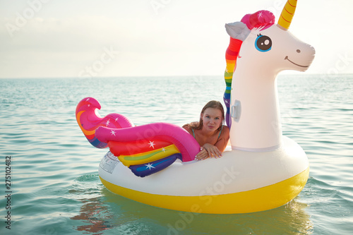 Lifestyle portrait of young beautiful girl with inflatable pool unicorn at sunset