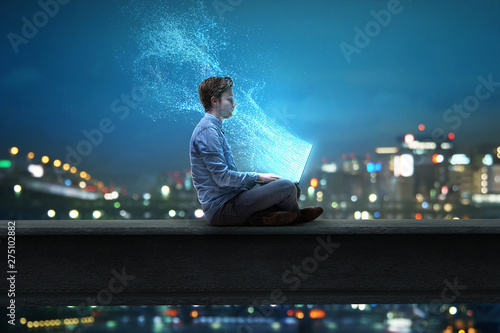 Mann sitzt am Notebook vor nächtlicher Stadt photo