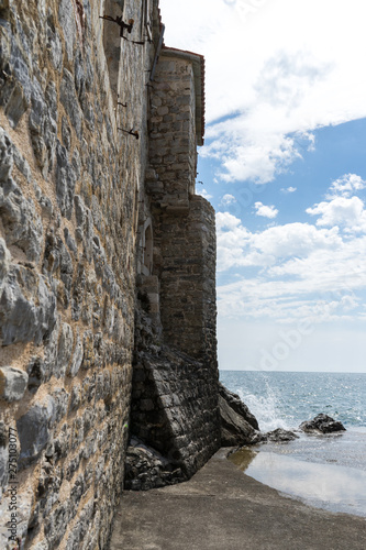 Old Town and Fort Wall at Adriatic Sea in Budva, Montenegro. Outside walls quiet sea hedging the beach. Blue sky with white cloud day. Old stone fortress
