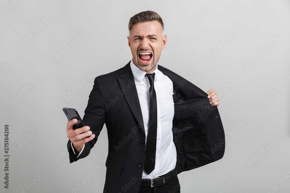 Image of delighted caucasian businessman in formal suit holding cellphone and celebrating victory