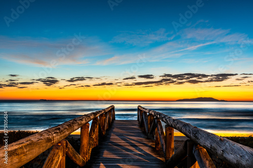 beautiful landscape with wooden walkway to seascape beach at sunrise with blue and orange sky and island in the background photo