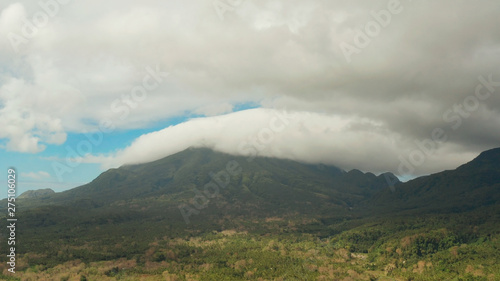 Aerial view of mountains covered rainforest, trees. Camiguin, Philippines. Mountain landscape on tropical island with mountain peaks covered with forest. Slopes of mountains with evergreen vegetation.