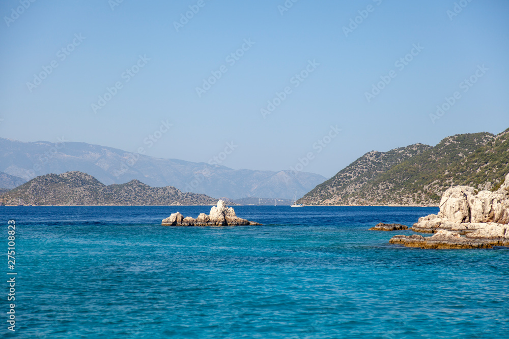 A view of the blue sea with some big mountains and a small rocky island in the middle of it
