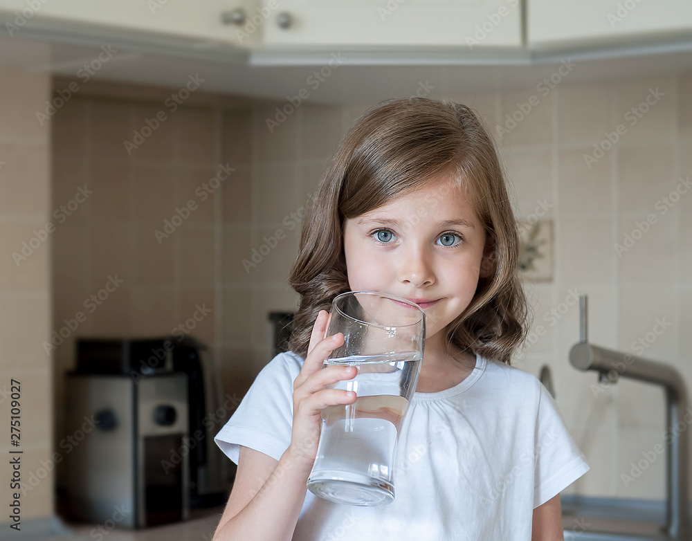 Little child is drinking clean water at home, close up. Caucasian cute girl with long hair is holding a water glass in her hands. Taking care of own health. Concept of healthy lifestyle, good habit