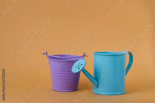 Toy blue watering can and purple bucket on an orange background. © IrinaK