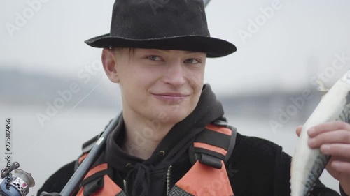 Portait young confident happy fisherman wearing a cap with a brim in the early morning catch fand showing fish looking to camera. Fun or joke. Raffle or incredible. photo