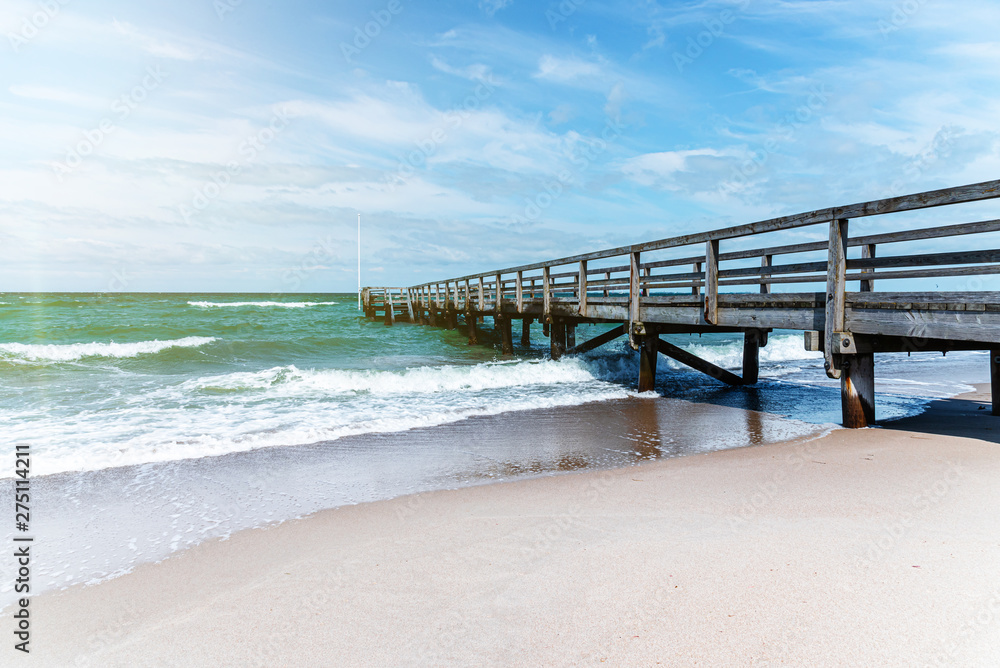 wooden pier on sand beach against ocean and blue summer sky on sunny day