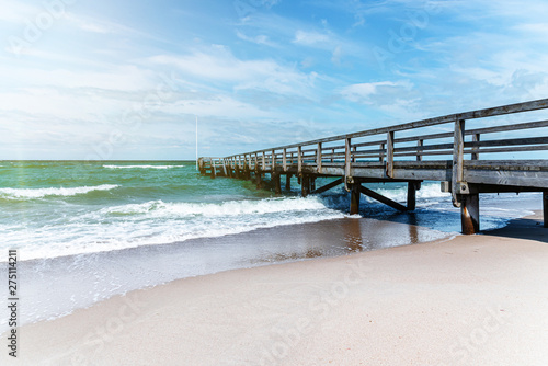 wooden pier on sand beach against ocean and blue summer sky on sunny day