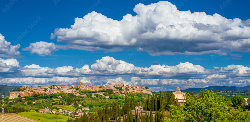 View of Orvieto medieval historic center with its characteristic ancient buildings made of tuff stone, beautiful clouds above and the Umbria green countryside