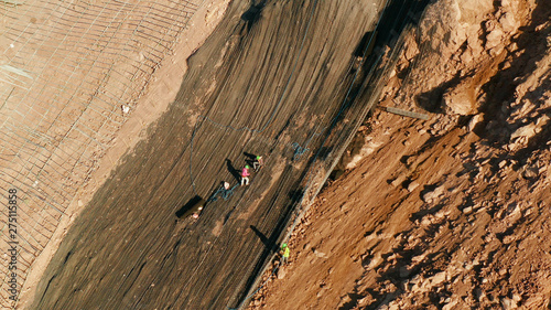 Fotografie Workers strengthen the slope of the mountain with metal mesh preventing rockfall and landslide on the road, above view