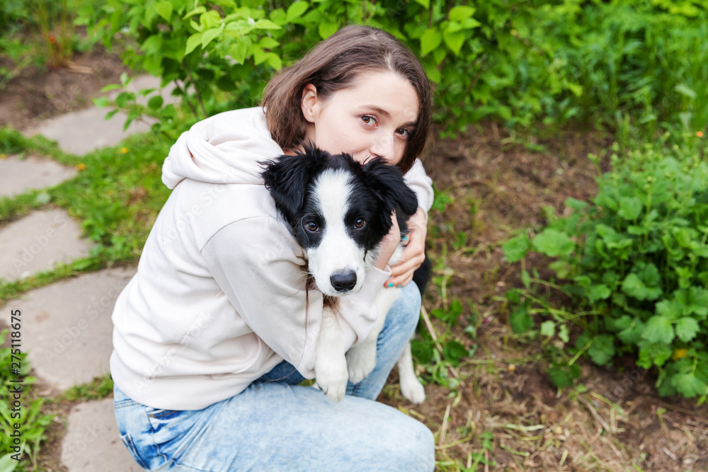 Smiling young attractive woman embracing cute puppy dog border collie in summer city park outdoor background. Girl huging new lovely member of family. Pet care and animals concept