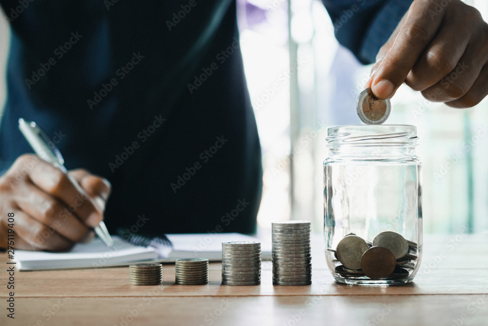 Men are Saint documents about save money and put coin in glass jar on desk. Men are Saint documents about save money and put coin in glass jar on desk.