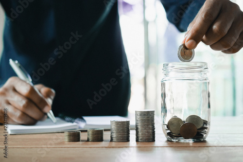Men are Saint documents about save money and put coin in glass jar on desk.
