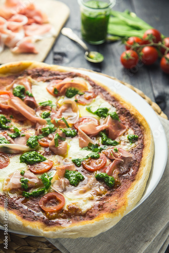 Prosciutto and pesto pizza with cherry tomatoes on a dark wooden background.