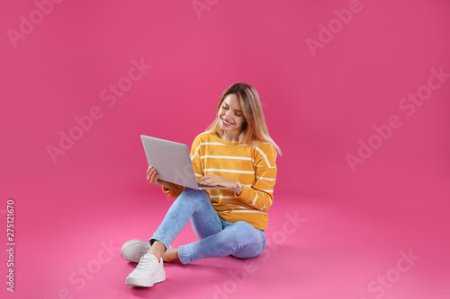 Young woman in casual outfit with laptop sitting on color background