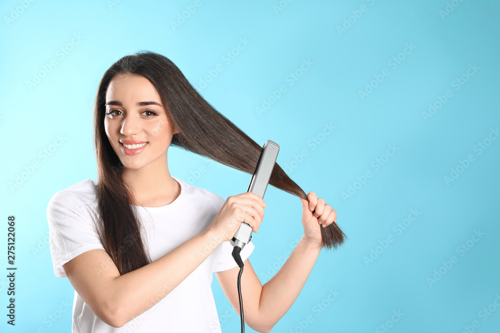 Happy woman using hair iron on color background. Space for text Happy woman using hair iron on color background. Space for text