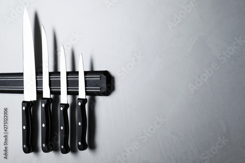 Magnetic holder with set of knives on grey stone background. Space for text