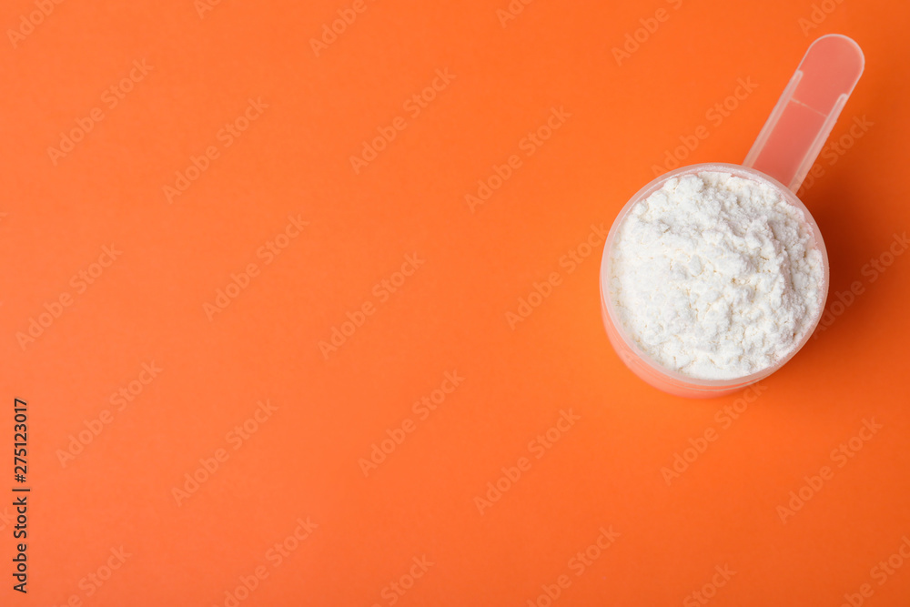 Scoop of protein powder on orange background, top view with space for text