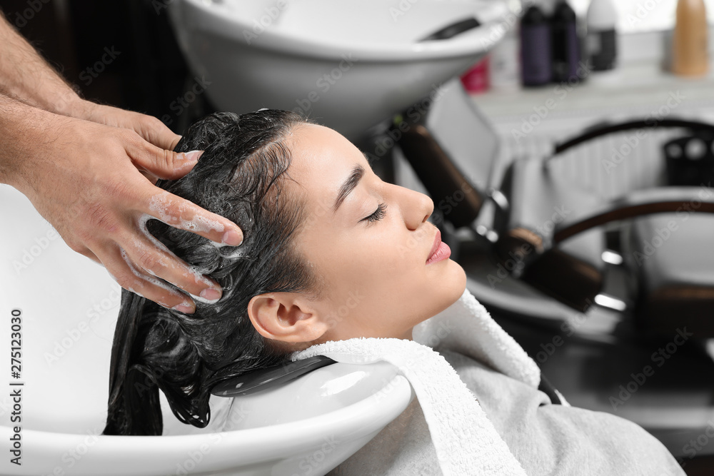 Fototapeta premium Stylist washing client's hair at sink in beauty salon