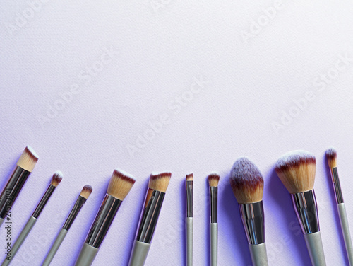 Many different makeup brushes on lilac background, flat lay. Space for text