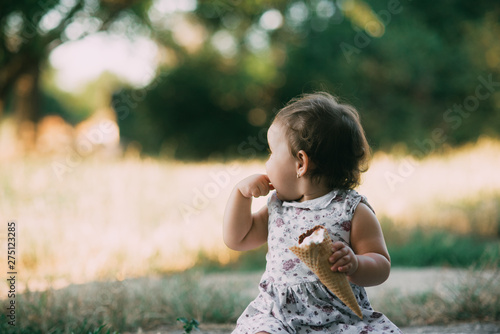 Little, charming girl in a dress in the summer eating ice cream at sunset