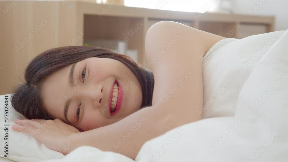Asian woman smiling lying on bed in bedroom, Beautiful japanese female using relax time after wake up at home. Lifestyle women using relax time at home concept. Slow motion shot. Asian woman smiling lying on bed in bedroom, Beautiful japanese female using relax time after wake up at home. Lifestyle women using relax time at home concept. Slow motion shot.