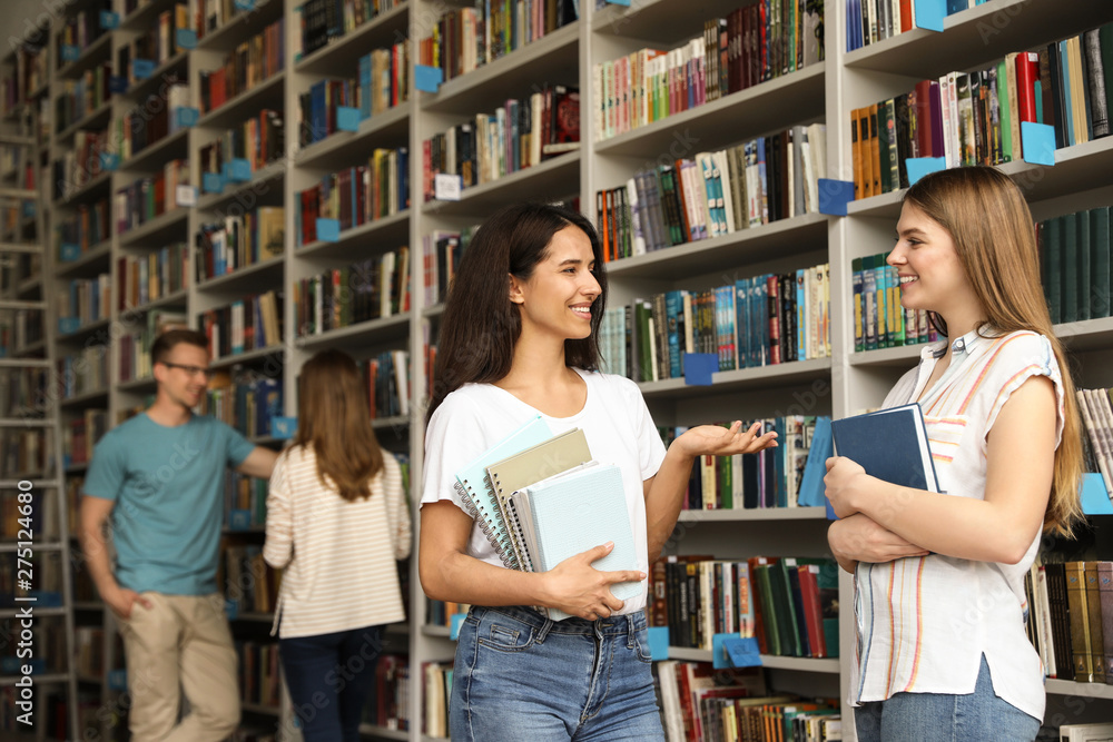 Young people standing near bookshelves in library Young people standing near bookshelves in library